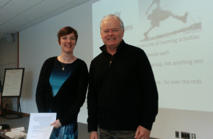 Beth Cougler Blom and David Stevenson standing in front of a screen and smiling at the camera