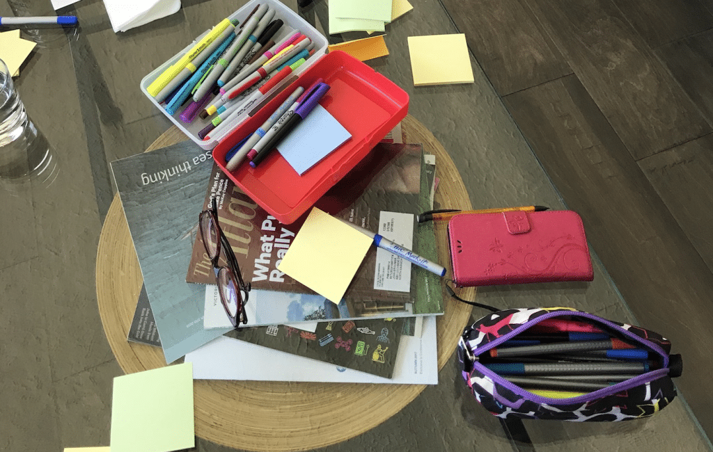 Pens and sticky notes and magazines strewn on a glass table.